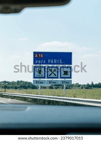 Vers Paris sign on France's A16 highway directs travelers toward Paris while indicating upcoming amenities like gas stations, restaurants, and coffee shops 80 km ahead