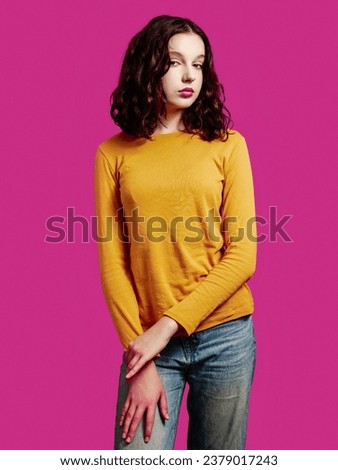 Yong teenager girl simple pose. Rich saturated red color background. Model or influencer studio shot. Beauty and fashion. Slim body type calm face expression.