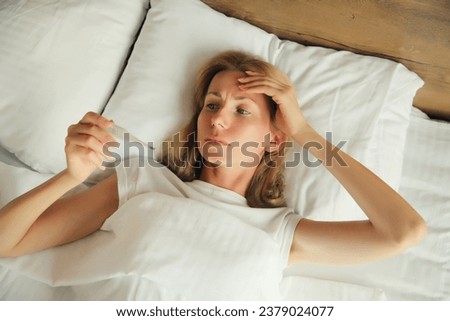 Sick woman measuring checking body temperature looking at thermometer while lying on bed at home Royalty-Free Stock Photo #2379024077
