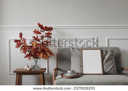 Red oak tree leaves, branches in vase. Linen midcentury sofa with cup of coffee. Blank wooden picture frame mockup. Little white pumpkins, old side table. Autumn interior. Thanksgiving, Halloween.
