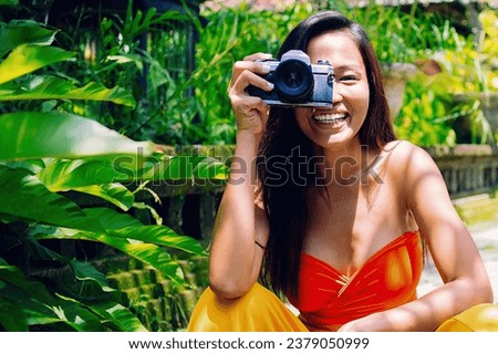 Happy female traveller sitting in tropical gardens with camera