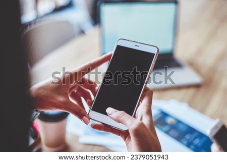 Woman sitting at table browsing cellphone in workplace