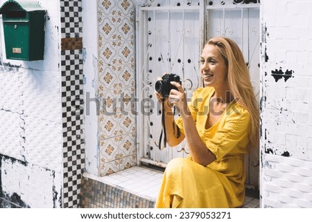 Young woman sitting next to old building and taking picture with photo camera