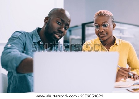 Black coworkers using laptop while having discussion in cafe