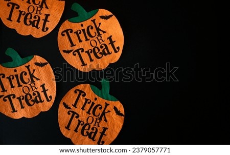 Creative, cheerful, elegant and aesthetic Halloween background with cutouts of pumpkins with green stems black trick or treat lettering, bats and dark black background. Top view, horizontal photograph