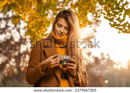Pretty young woman photography enthusiast holding analog camera in hand, sunset in autumn in park  