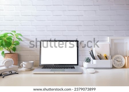 Home office interior. Computer laptop, picture frame, coffee cup, notebook and flower pot on white table.