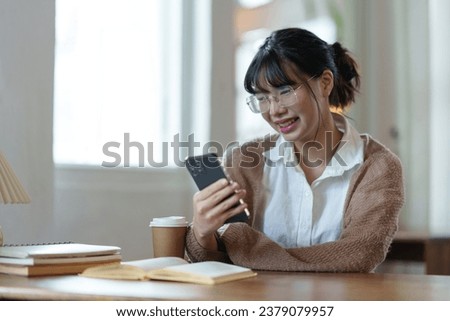 Positive asian young female accountant using a smartphone at her office desk. Woman relaxing on her mobile application.