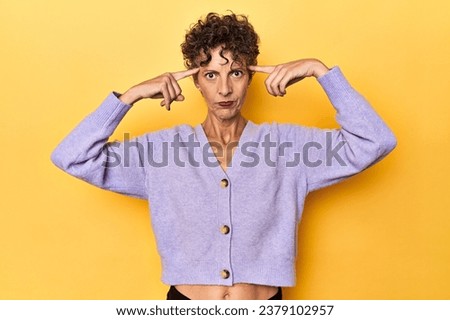 Mid-aged caucasian woman on vibrant yellow focused on a task, keeping forefingers pointing head.