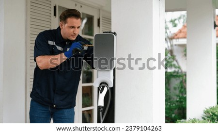 Qualified technician install home EV charging station, providing maintenance service for electric vehicle's battery charging platform at home. EV car technology for residential utilization. Synchronos Royalty-Free Stock Photo #2379104263