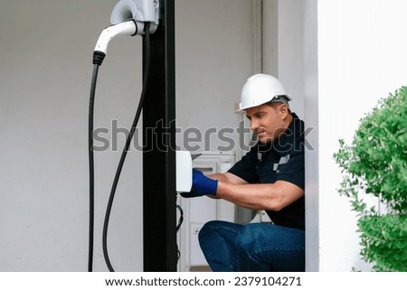 Qualified technician install home EV charging station, providing maintenance service for electric vehicle's battery charging platform at home. EV car technology for residential utilization. Synchronos Royalty-Free Stock Photo #2379104271