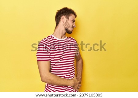 Young Caucasian man on a yellow studio background suffering a back pain.
