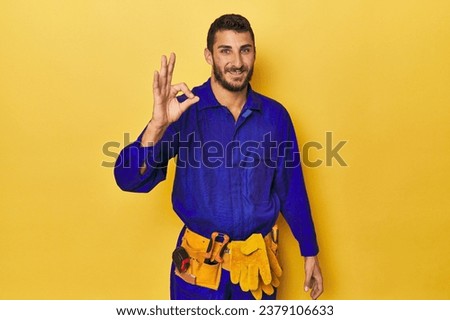 Young Hispanic man in a blue jumpsuit Young Hispanic man in a blue jumpsuitcheerful and confident showing ok gesture. Royalty-Free Stock Photo #2379106633