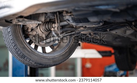 Drive shaft assembly or CV joint axle and wheel. Bottom view of car suspension. Old car on hydraulic lift during maintenance in auto repair shop Royalty-Free Stock Photo #2379114057