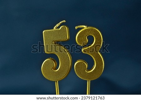 close up on the gold number fifty-third candle on a dark background.