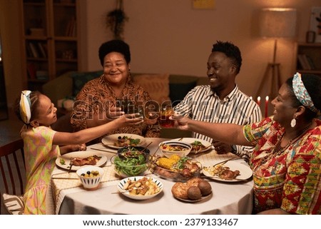Little girl clinking glasses with family dinner at Kwanzaa holiday dinner