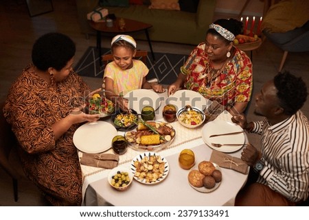 Black family celebrating Kwanzaa holiday at home, eating traditional dishes and talking