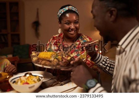 Smiling Black woman offering dish to husband at family Kwanzaa dinner
