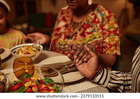 Hands of Black people hold hands and praying before eating traditional Kwanzaa dinner