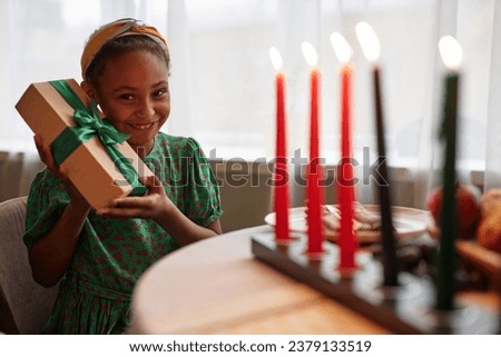 Portrait of excited preteen girl shaking Kwanzaa gift from her family