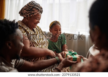 Smiling Black girl accepting present from family when celebrating Kwanzaa at home