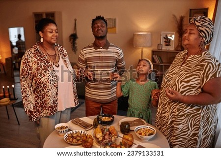 Black family closing eyes and hold hands when praying before eating Kwanzaa dinner