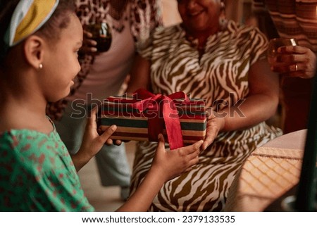 Grandmother giving Kwanzaa present to little girl when celebrating at home