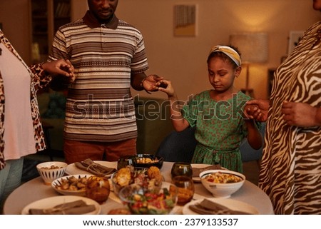 Black family hold hands and praying before eating dinner served for Kwanzaa celebration