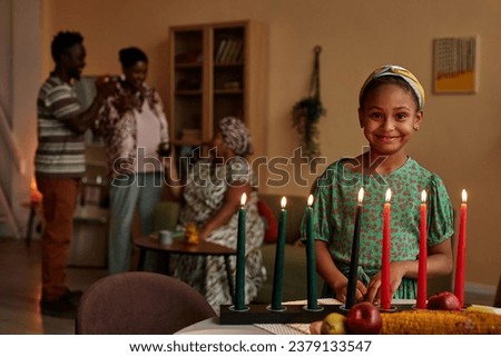 Smiling Black girl standing at candle holder prepared for Kwanzaa celebration