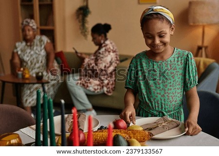 Cheerful preteen Black girl enjoying preparing everything for Kwanzaa celebration