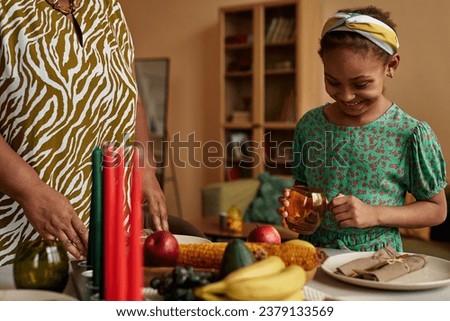 Cheerful Black little girl helping grandmother setting table for Kwanzaa dinner