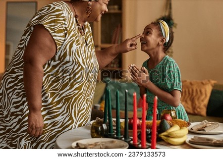 Grandmother touching nose of excited little granddaughter when they are preparing for Kwanzaa celebration