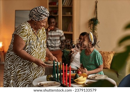 Smiling grandmother bringing plates to table served for kwanzaa holiday