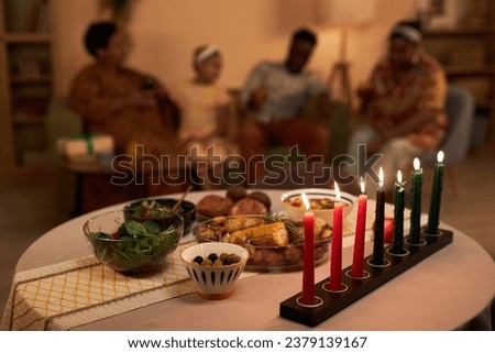 Colorful burning candles and tasty dishes on table in living room of family celebrating Kwanzaa