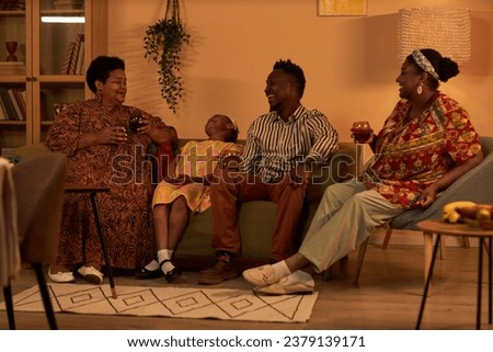 Happy Black family enjoying soft drinks, talking and joking around when celebrating Kwanzaa at home