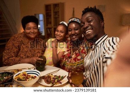 Happy Black man taking selfie with family when sitting at table served for Kwanzaa celebration