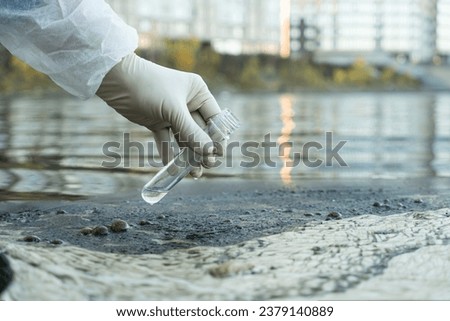 female ecologist in a protective glove holding a test tube with water from a city river Royalty-Free Stock Photo #2379140889