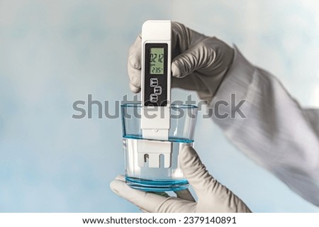 pH meter in hands with gloves, glass of water on a blue background. Measurement of the characteristics of drinking water. The hardness of the water. poor water quality. high values of salt impurities Royalty-Free Stock Photo #2379140891