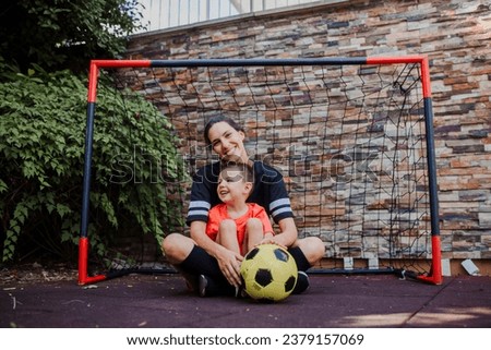 Mom playing football with her son, dressed in football jerseys. The family as one soccer team. Family sports activities outside in the backyard or on the street.