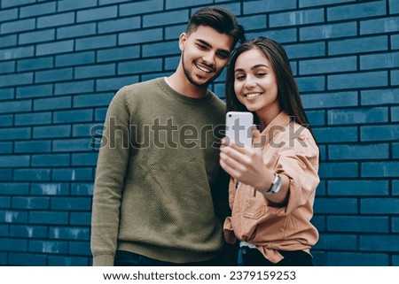 Cheerful couple in love dressed in casual posing for selfie on smartphone camera standing together