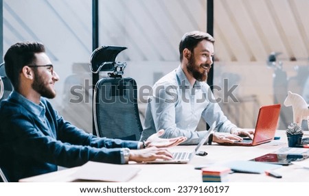 Cheerful colleagues interacting in office with laptops