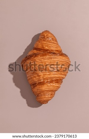 Multi-layered lush croissant on a beige background with hard light Royalty-Free Stock Photo #2379170613