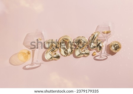 Happy New Year festive background, golden inflatable balls in shape 2024 on pale pink, shiny wine glasses, Christmas transparent ball and mirror disco ball. Shadows and lights, Star filter effect