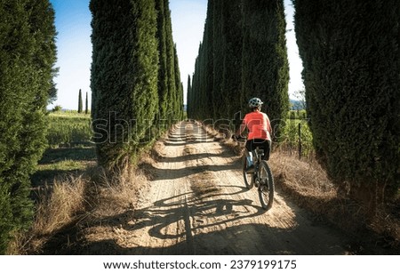nice senior woman riding her electric mountain bike in a cypress avenue in the Ghianti Area of Tuscany,Italy Royalty-Free Stock Photo #2379199175