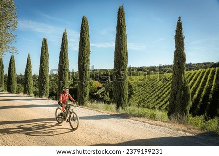 nice senior woman riding her electric mountain bike in a cypress avenue in the Ghianti Area of Tuscany,Italy Royalty-Free Stock Photo #2379199231