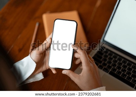 Top view of a woman using her smartphone while sitting at her working desk. A white-screen smartphone mockup. close-up image Royalty-Free Stock Photo #2379202681