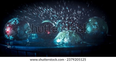 New year and Christmas concept. Glass bauble dropped into water or water splash on dark foggy background. Selective focus.