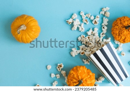 Stripped box full of popcorn and small decorative pumpkinson a yellow background with copy space. Halloween banner. Autumn or fall movie concept.  Movie night concept. Watching TV themed.