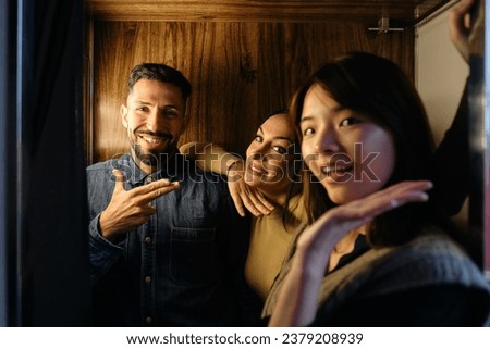Three friends are inside a photobooth, creating playful and humorous expressions as they pose for pictures Royalty-Free Stock Photo #2379208939