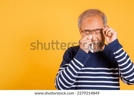 Asian elder man crying raise glasses with tissue wipe red eyes studio shot isolated on yellow background, Portrait senior old man sad wiping away his tears, Upset depressed lonely Royalty-Free Stock Photo #2379214849